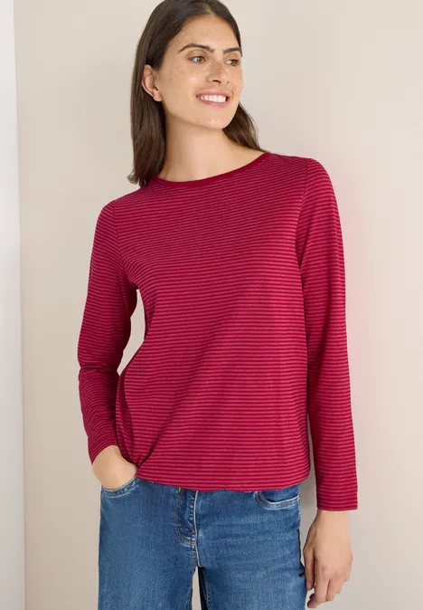 Frau mit rot gestreiftem Langarmshirt und Jeans lächelt.